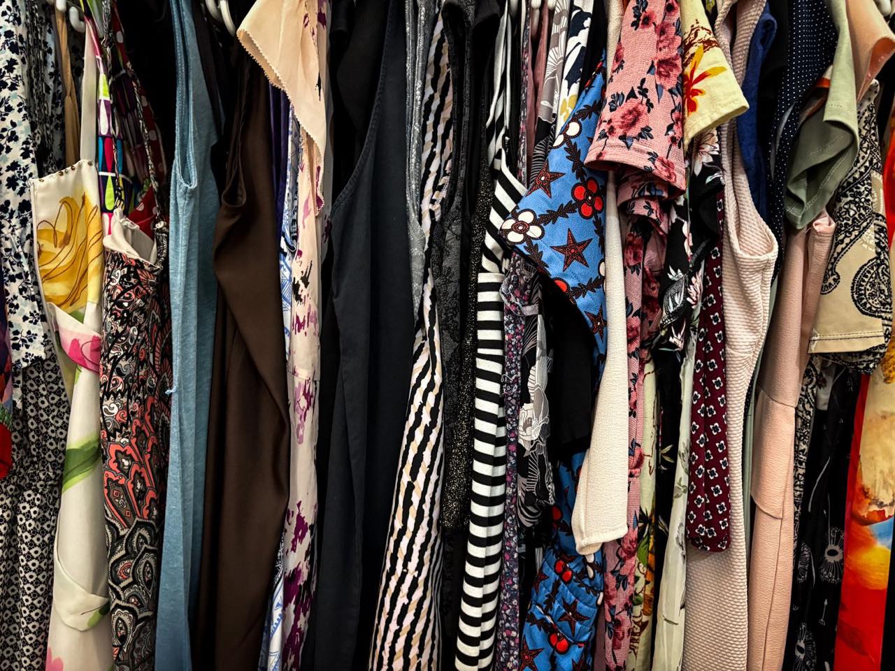 A densely packed rack of patterned vintage dresses and blouses