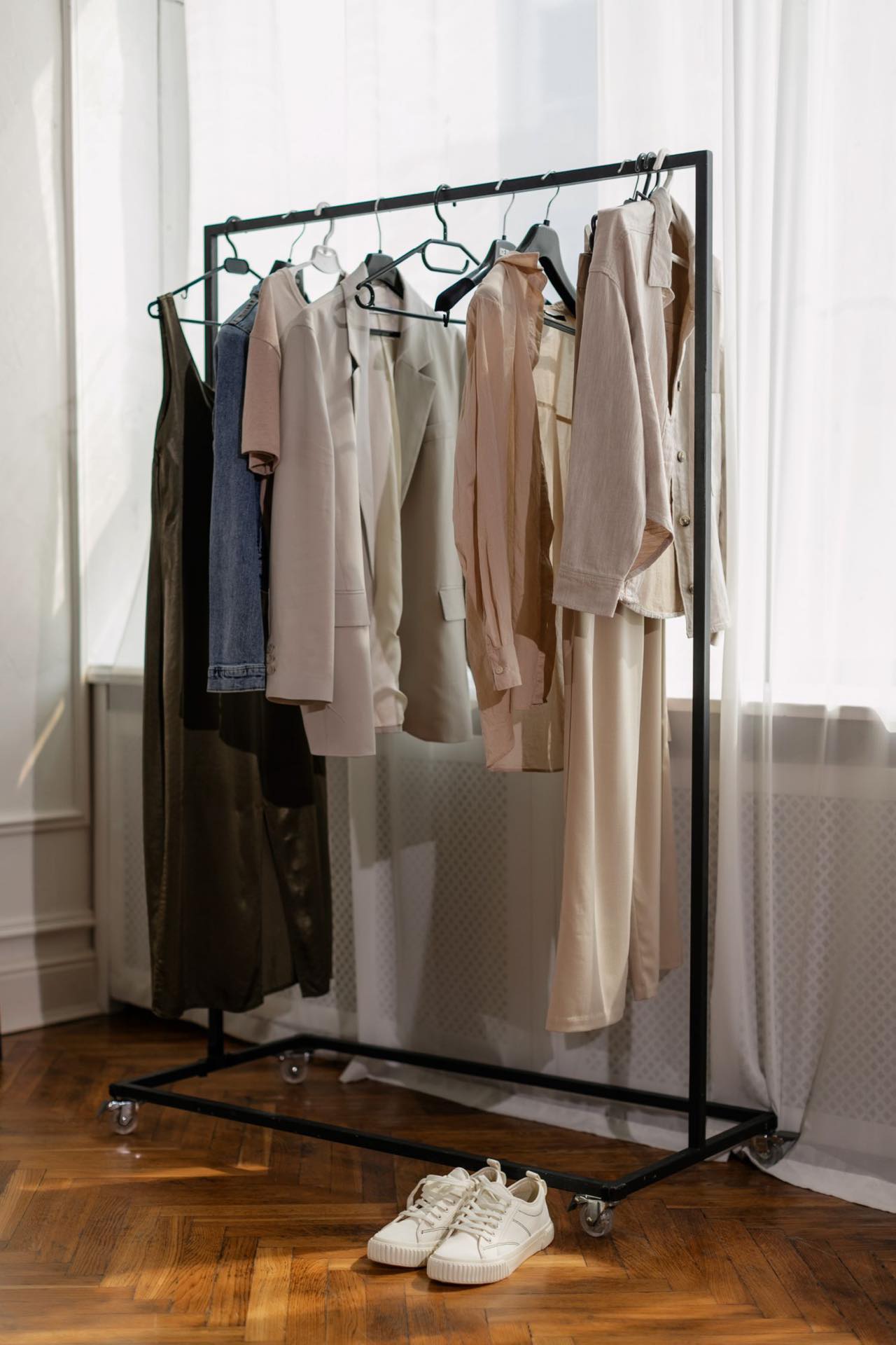 A rack of neutral-toned vintage pieces beside a window, with a pair of shoes on the parquet floor